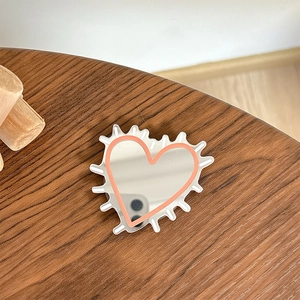 Close-up of heart-shaped mirror phone grip with pink border on wooden desktop