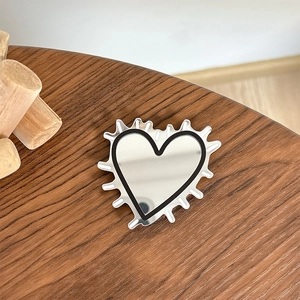 Macro detail of heart-shaped phone grip with silver mirror finish on dark wood texture