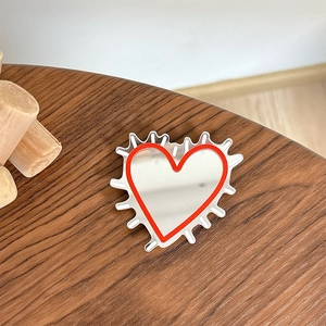 Detail view of heart-shaped phone mirror stand with red doodle edges on wooden desk