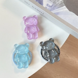 Glitter bear phone grip stands in purple, light blue and black on a white surface