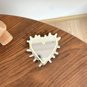 Detail of silver heart mirror phone grip with Y2K jagged edges on a wooden surface
