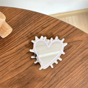 Macro detail of heart-shaped mirror phone grip with purple lines on wood background