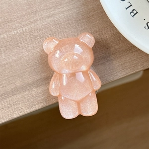Close-up of a pink resin glitter bear phone grip on a minimalist wooden table surface