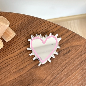 Close-up of heart-shaped phone grip mirror with pink trim on dark wood surface