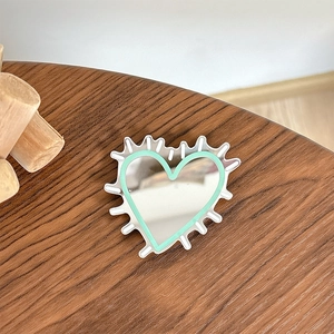 Detail of heart mirror phone grip with mint green edge on a dark wooden surface