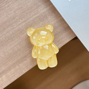 Close-up of a translucent bright yellow glittery bear phone grip on a wooden desk