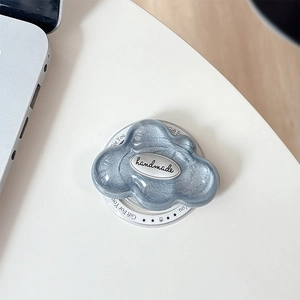 Macro detail of glittery cloud phone grip with handmade silver emblem on white coaster