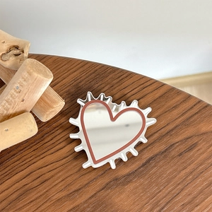 Close-up of heart-shaped makeup mirror with red border on a rustic wooden table