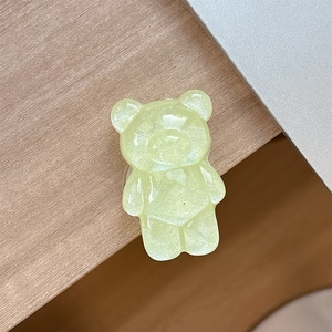 Detail of a light yellow glittery gummy bear phone grip on a wooden office desk