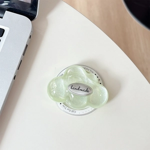Detail of glittery green cloud phone grip with handmade silver emblem on desk