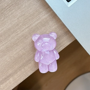 Close-up of a glittery purple resin bear phone grip on a minimalist wooden desktop