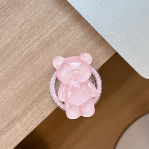 Pink glitter bear phone grip with pearl base on a wooden desk, close-up view
