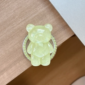Detail of light green bear phone grip with pearl border on a wooden table surface