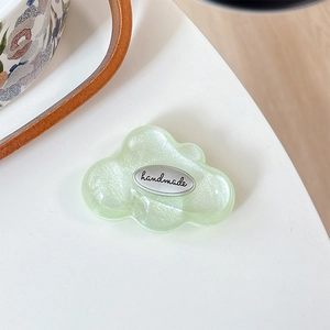 Close-up of a pearlescent light green cloud phone grip with a silver handmade metal tag