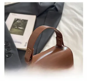 Detail of the brown leather handbag handle featuring reinforced triangular stitching and rings