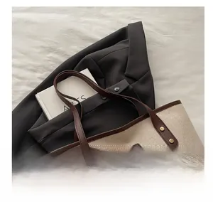 Close-up of beige woven tote bag with brown leather handles and gold rivet details