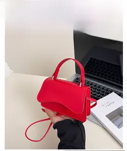 Detail of red mini crossbody bag with wavy flap and solid handle on office desk