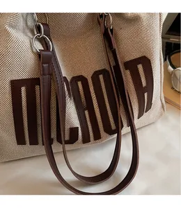 Detail of canvas tote bag with brown leather straps and smooth metallic hardware rings