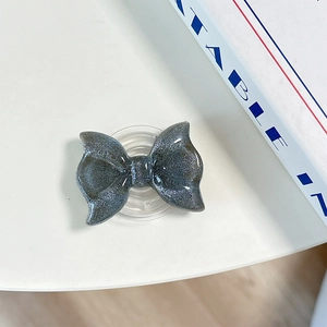 Close-up of a dark grey glittery bow Griptok phone holder with transparent base