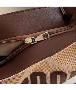 Detail of silver smooth hardware zipper on beige canvas and brown leather tote bag