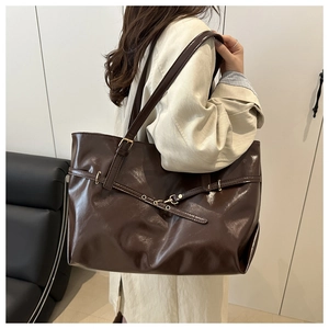 Detail of dark brown tote bag with glossy leather texture and metal buckle accents
