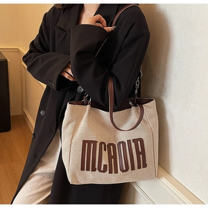 Close-up of canvas tote bag with brown leather letter applique and metal chain detail