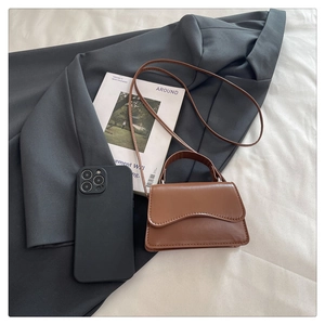 Detail view of a brown mini handbag featuring a wave-edge flap and vintage PU leather finish