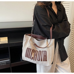 Detail of canvas tote bag showing large brown leather letter patch and metal chain strap