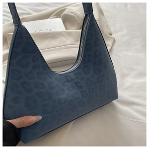 Detail of blue leopard print underarm bag with zipper closure on white fabric background