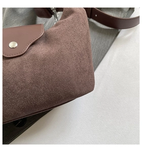 Close-up of brown suede shoulder bag with metallic buckle and leather strap details