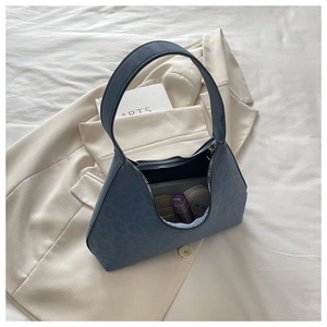 Details einer blauen Hobo-Tasche mit Leopardenmuster und Kosmetik auf weißem Grund