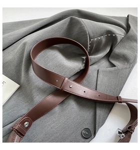 Detail of brown leather strap with metallic rivets and stitching on a grey blazer