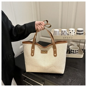 Close-up of the beige canvas tote bag showing brown leather handles and golden rivets