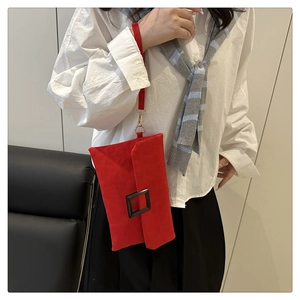 Detail of red envelope clutch with black square buckle and wristlet strap on a model