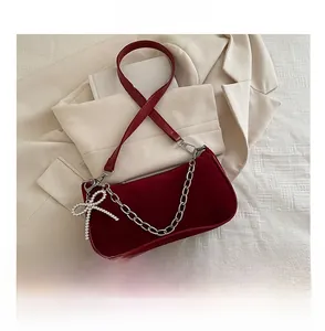 Detail of red velvet shoulder bag featuring silver chain and rhinestone bow ornament