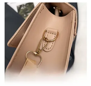 Detailed close-up of light gold metal lobster clasp and hardware on beige square bag