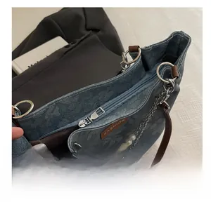 Detail view of smooth metal zipper and pearl chain on vintage floral denim shoulder bag