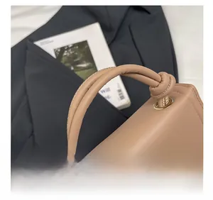 Close-up of beige leather handbag with knotted strap and circular metal hardware