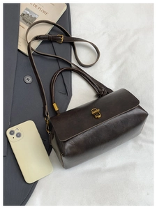 Close-up of deep brown vintage handbag with gold clasp and leather texture on gray fabric