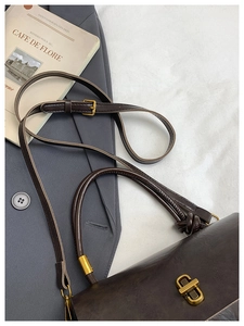 Detailed view of coffee brown vintage handbag with gold clasp on a grey suit jacket