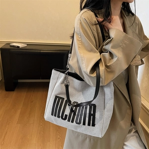 Minimalist beige canvas tote bag with black leather straps and embroidered lettering