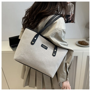 Close-up of minimalist canvas tote bag with black leather trim and small logo detail
