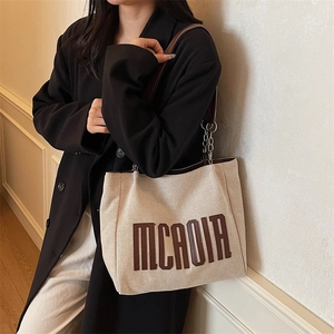 Beige canvas tote bag with brown MCAOIA lettering and chain strap shown on a model