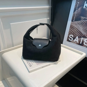 Minimalist black suede tote bag with leather flap and metallic pendant on display