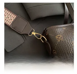 Detail of gold metal hook and woven strap on a brown pebbled leather bucket bag
