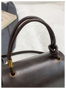 Detail of dark brown leather handbag featuring golden hardware and leather knot handle