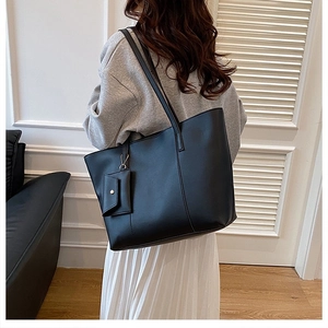 Detail of a large black matte PU leather tote bag with matching charm pouch on a model