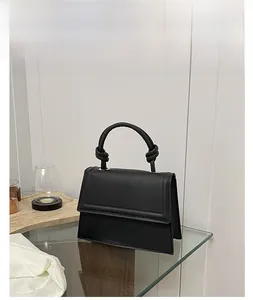 Detail view of black leather handbag featuring knot handle design and gold hardware