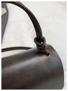 Detail of dark brown retro square bag showing leather texture and knotted shoulder strap