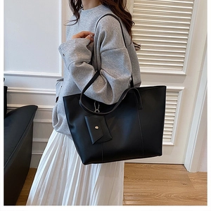 Detail view of large black tote bag and matching pouch on a model in a minimalist room